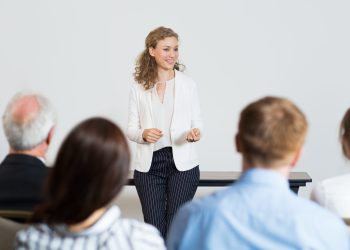 Portrait of successful young businesswoman speaking in front of audience at conference, making presentation to colleagues